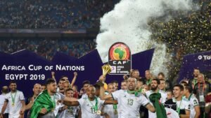 Les joueurs algériens célèbrent la victoire en Coupe d'Afrique des Nations 2019, levant le trophée au milieu des confettis et des fans enjoués dans le stade.
