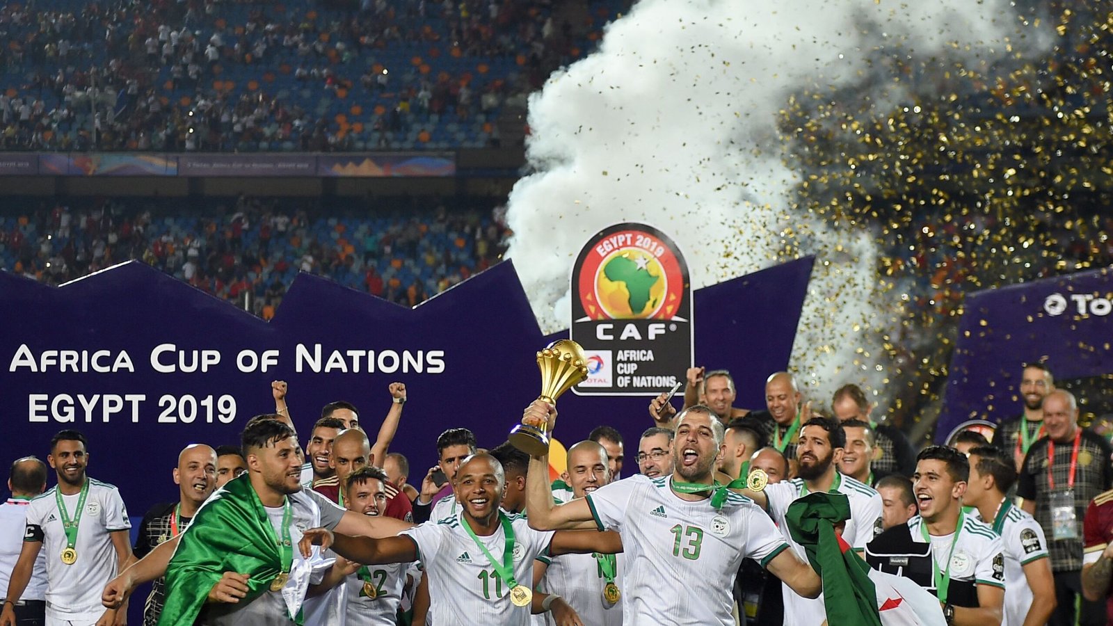 Les joueurs algériens célèbrent la victoire en Coupe d'Afrique des Nations 2019, levant le trophée au milieu des confettis et des fans enjoués dans le stade.