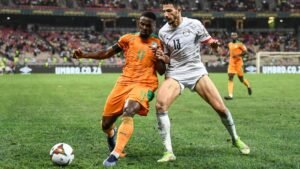 Ivory Coast’s player in orange battles for the ball with Egypt’s player in white during a tense AFCON match, with fans in the background.