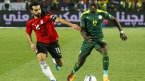 Mohamed Salah en tenue rouge de l'Égypte dribble Sadio Mané en tenue verte et jaune du Sénégal lors d'un match intense.
