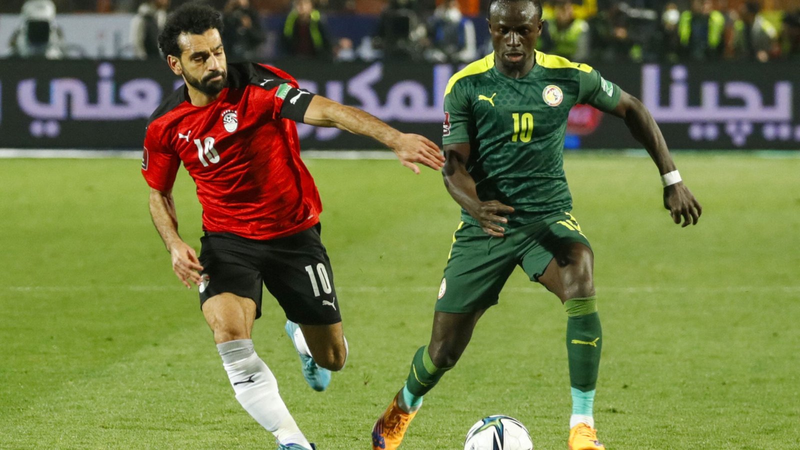 Mohamed Salah en tenue rouge de l'Égypte dribble Sadio Mané en tenue verte et jaune du Sénégal lors d'un match intense.