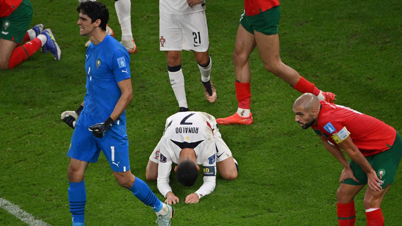 Le gardien marocain Yassine Bounou célèbre tandis que le Portugais Cristiano Ronaldo s'agenouille en signe de défaite, avec des joueurs marocains à proximité, lors d'un match de Coupe du Monde tendu.