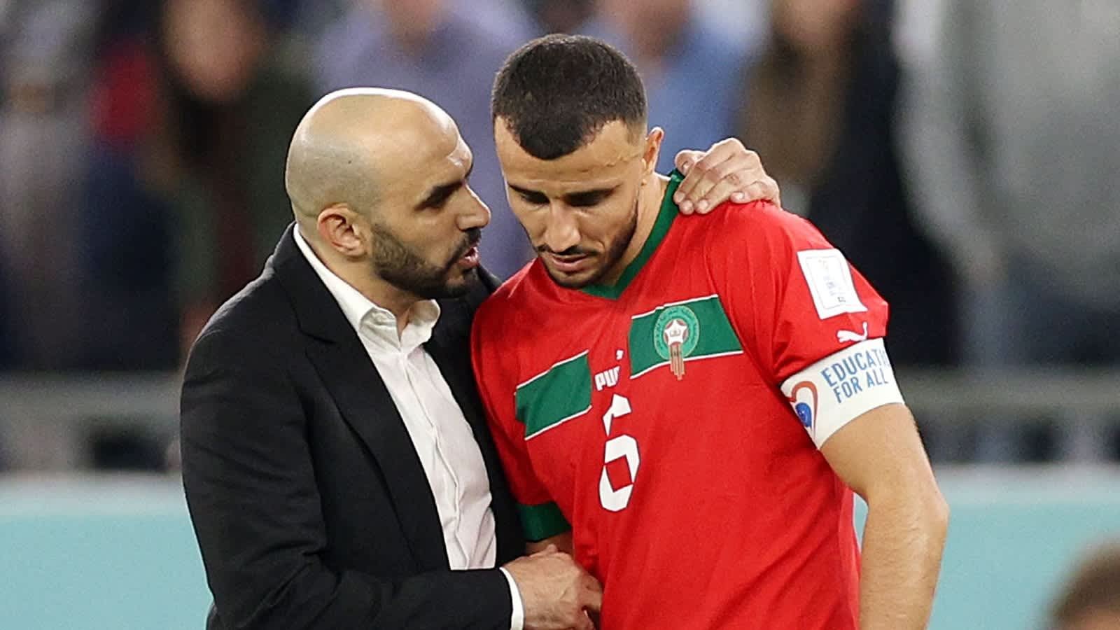 Coach Walid Regragui speaks to captain Romain Saïss, wearing Morocco's red kit, during a tense moment on the pitch.