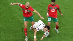 Moroccan defenders, wearing red and green kits, challenge a falling opponent during a heated World Cup match.