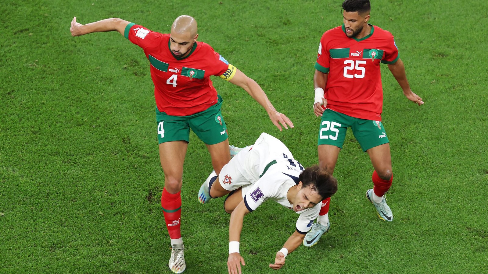 Moroccan defenders, wearing red and green kits, challenge a falling opponent during a heated World Cup match.
