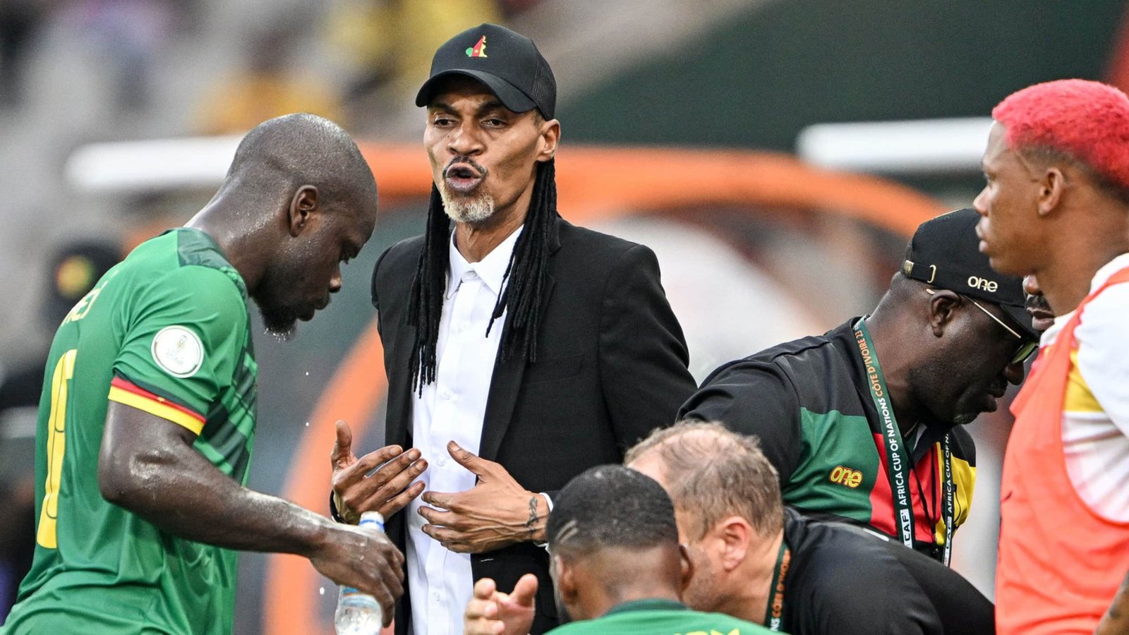 L'entraîneur de l'équipe nationale du Cameroun discute avec passion de la stratégie avec ses joueurs pendant un match, illustrant l'esprit d'équipe et la concentration.