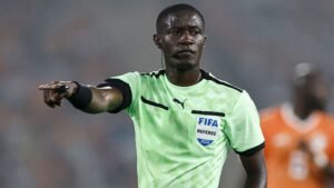 حكم الفيفا يرتدي الطقم الأخضر الزاهي، يشير خلال مباراة مشحونة، مع وجود لاعبين في الخلفية، مما يظهر حدة المنافسة.