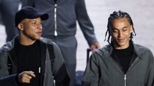 Mbappé et un coéquipier partagent un moment léger en marchant, tous deux vêtus de tenues décontractées grises, montrant une atmosphère détendue avant le match.