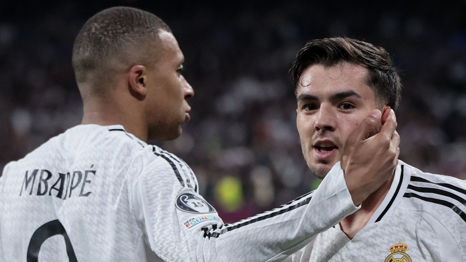 Kylian Mbappé embraces a teammate in a Real Madrid kit, celebrating during a UEFA tournament match, showcasing teamwork and excitement.