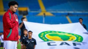 Moroccan player stands with a solemn expression during the national anthem, with a CAF flag prominently displayed in the background.