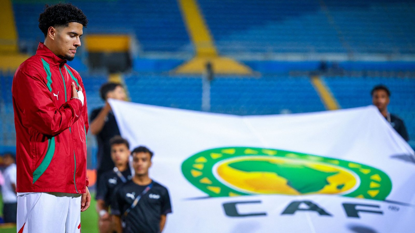 Moroccan player stands with a solemn expression during the national anthem, with a CAF flag prominently displayed in the background.