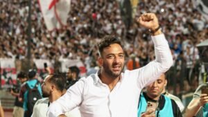 Celebrating fan in a white shirt raises a fist amidst a vibrant crowd, capturing the excitement of a Moroccan football match atmosphere.