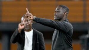 Entraîneur marocain faisant des gestes aux joueurs pendant l'entraînement, insistant sur la stratégie, un coéquipier en arrière-plan observant.