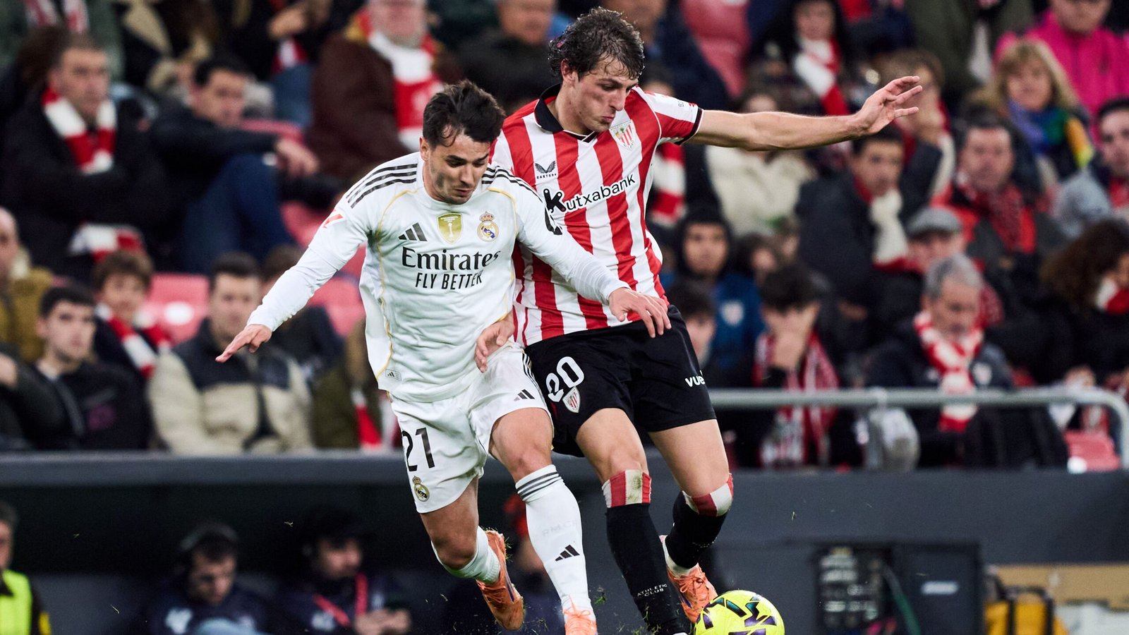 Real Madrid's player number 21 clashes with Athletic Bilbao's number 20, amid a lively crowd in a competitive match.