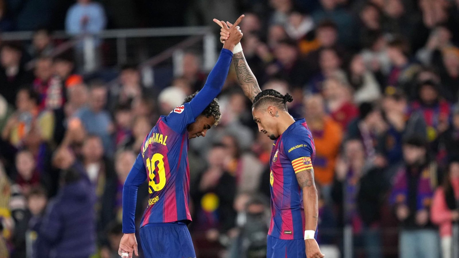 لاعبا برشلونة المحتفلان عثمان ديمبيلي ورفينيا يرفعان أيديهما بتناغم، محاطان بحماس جماهير كامب نو.