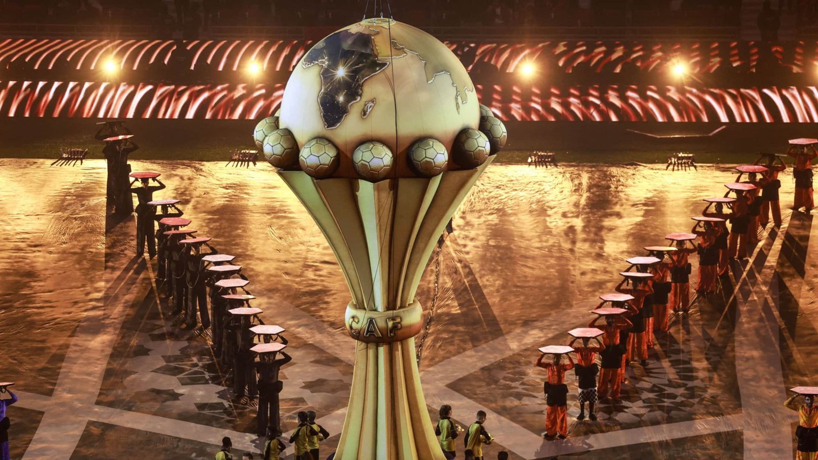 Celebratory AFCON trophy on display with performers in vibrant outfits, illuminating stage, showcasing the prestige of African football.