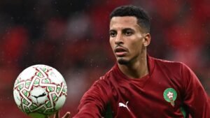 Moroccan player in maroon kit prepares to pass a decorative ball during a match, with rain droplets visible in the background.