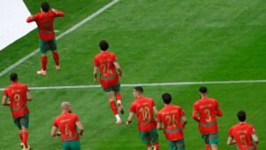 Morocco players celebrate on the pitch in their red and green kits, showing excitement after a goal during a key match.
