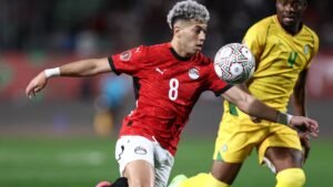 Egyptian midfielder wearing a red kit with number 8 attempts to control the ball, while a player in a yellow kit pressures him during a match.