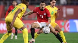 Le joueur égyptien numéro 11 dribble le ballon entouré de deux adversaires en jaune lors d'un match compétitif, montrant une intensité tactique.