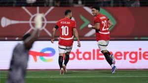 MSalah célèbre avec son coéquipier Harouni, tous deux en maillots rouges, après avoir marqué, avec des drapeaux marocains et des fans en arrière-plan.