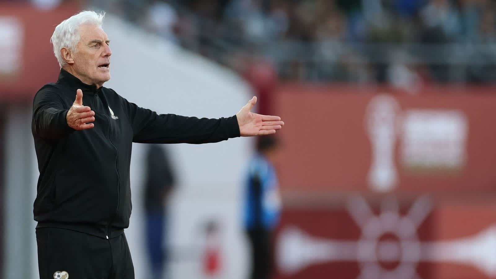 Walid Regragui gestures passionately on the touchline during a key match, dressed in a black tracksuit amidst a vibrant stadium backdrop.