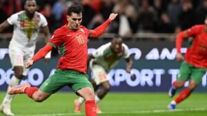 Moroccan player in red kit, number 10, executing a penalty kick against the backdrop of an opposing team in a competitive match.