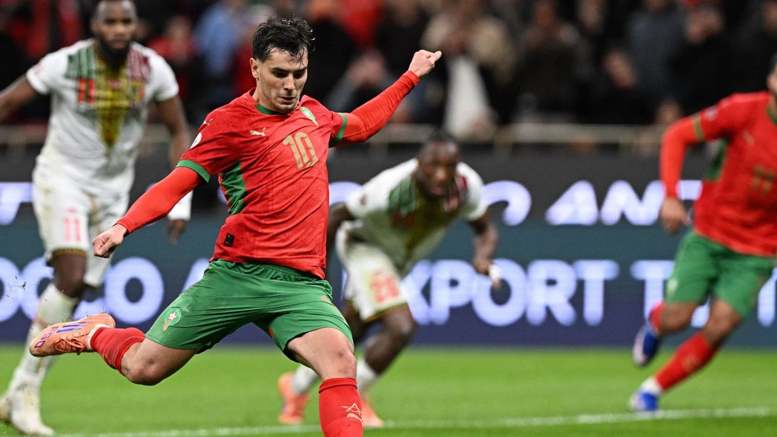 Moroccan player in red kit, number 10, executing a penalty kick against the backdrop of an opposing team in a competitive match.