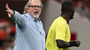 Coach animatedly gestures towards the referee during a match, emphasising his point in a dramatic display of expression.
