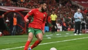 Moroccan player in a vibrant red and green kit, preparing to take a corner kick amid an enthusiastic crowd at the stadium.