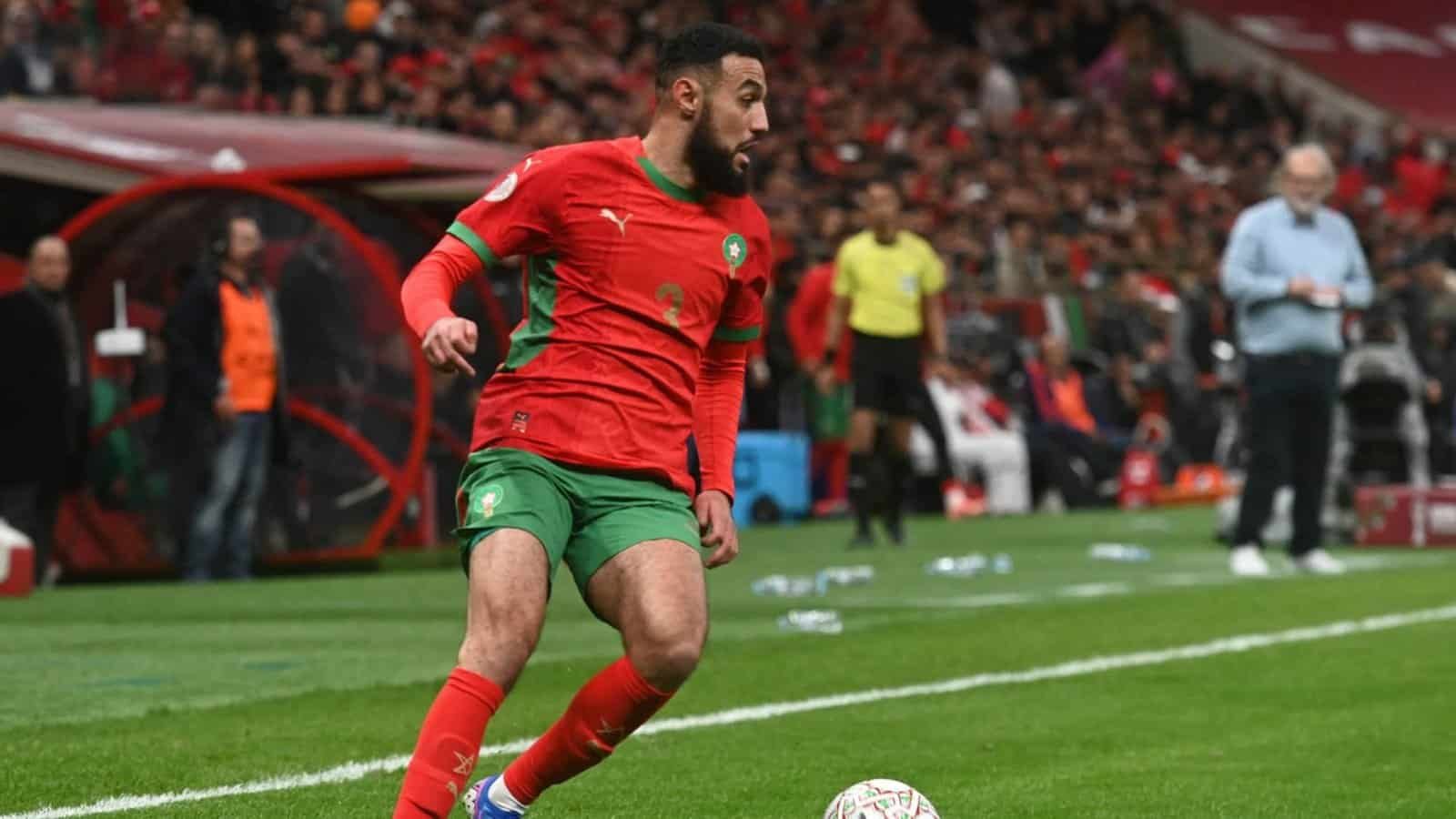 Moroccan player in a vibrant red and green kit, preparing to take a corner kick amid an enthusiastic crowd at the stadium.