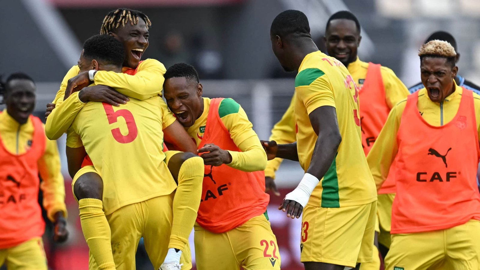Celebrating players in yellow jerseys rejoice after a goal, showcasing joy and teamwork during a CAF tournament match.