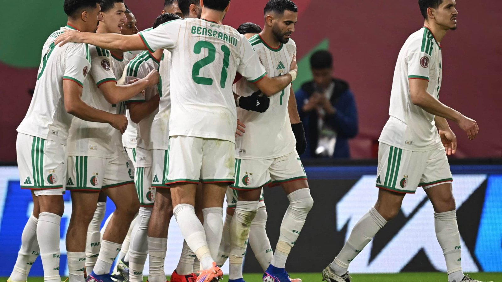 Les joueurs algériens célèbrent ensemble dans leurs tenues blanches rehaussées de vert, illustrant l'unité de l'équipe après un but marqué lors d'un match international.