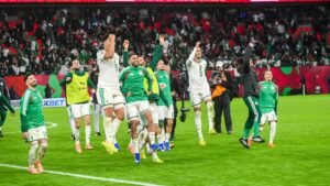 Algeria players celebrating enthusiastically on the pitch after a match, with a crowd of supporters in the background, showcasing team spirit.