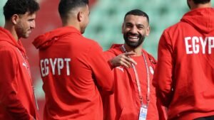 Egyptian players in red hoodies share a light moment during training, showcasing camaraderie ahead of an upcoming match.