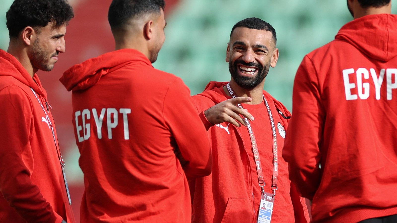 Egyptian players in red hoodies share a light moment during training, showcasing camaraderie ahead of an upcoming match.