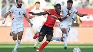Ugandan player in a red and yellow kit evades two Egyptian defenders in a dynamic tackle during a high-stakes match.