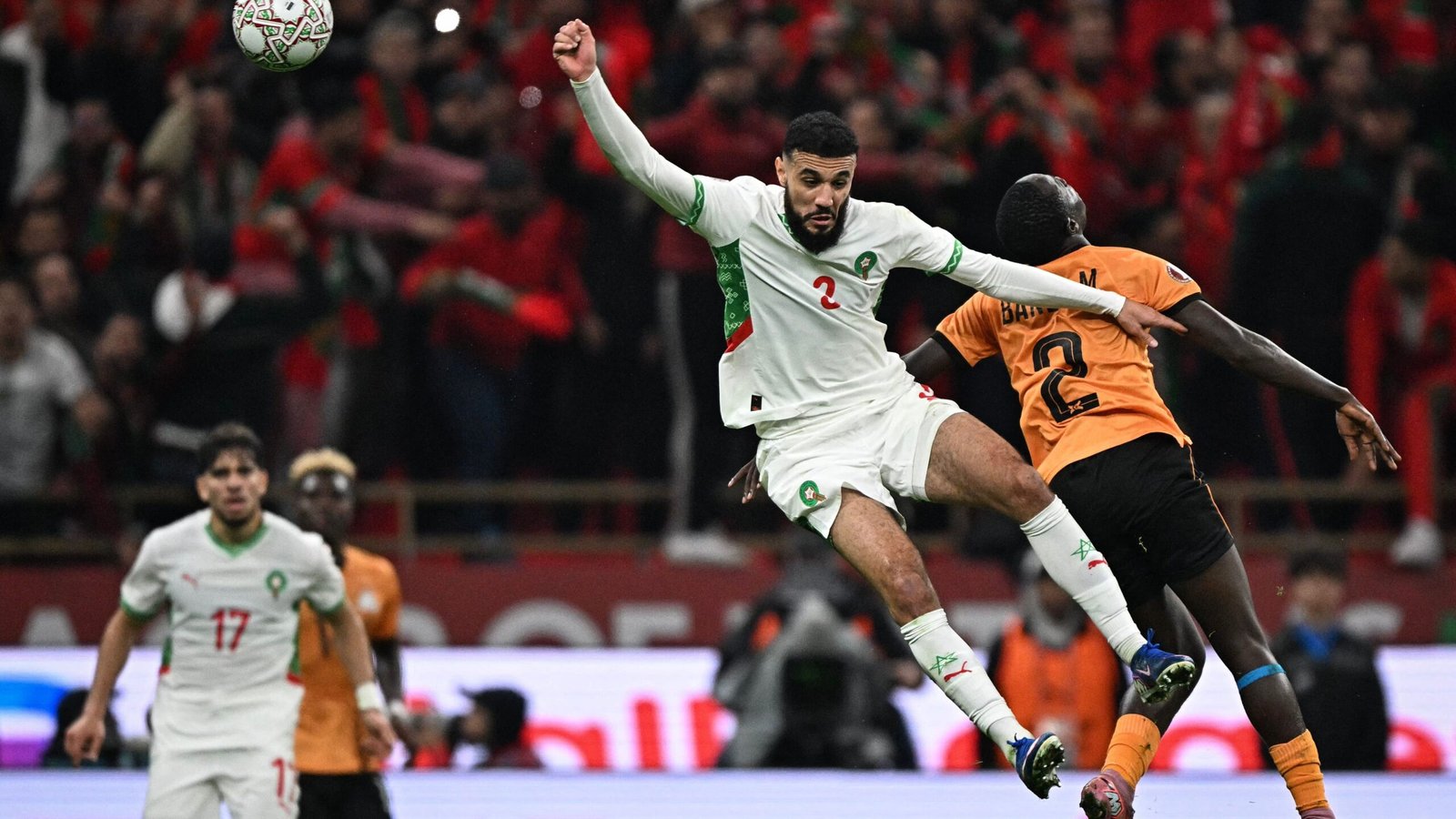 Moroccan players compete intensely during a match, with a player in a white kit evading an opposing player in orange.