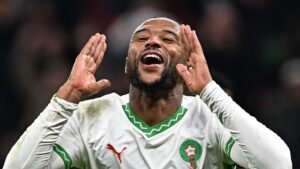 Moroccan player passionately celebrating, shouting with joy in a white kit featuring green accents, showcasing national pride.