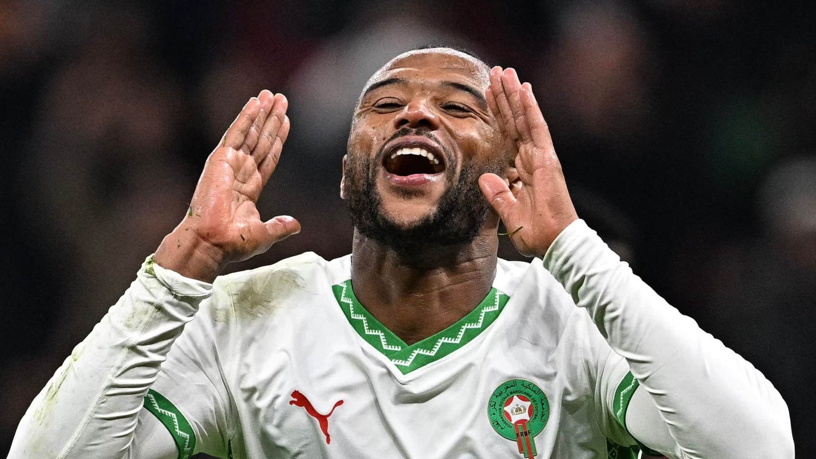 Moroccan player celebrating passionately, gesturing with hands, wearing the national team's white kit with green accents during a match.