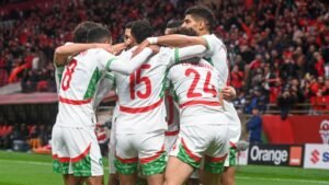 Moroccan players celebrate a goal in vibrant white kits with green and red accents, surrounded by cheering fans in a packed stadium.