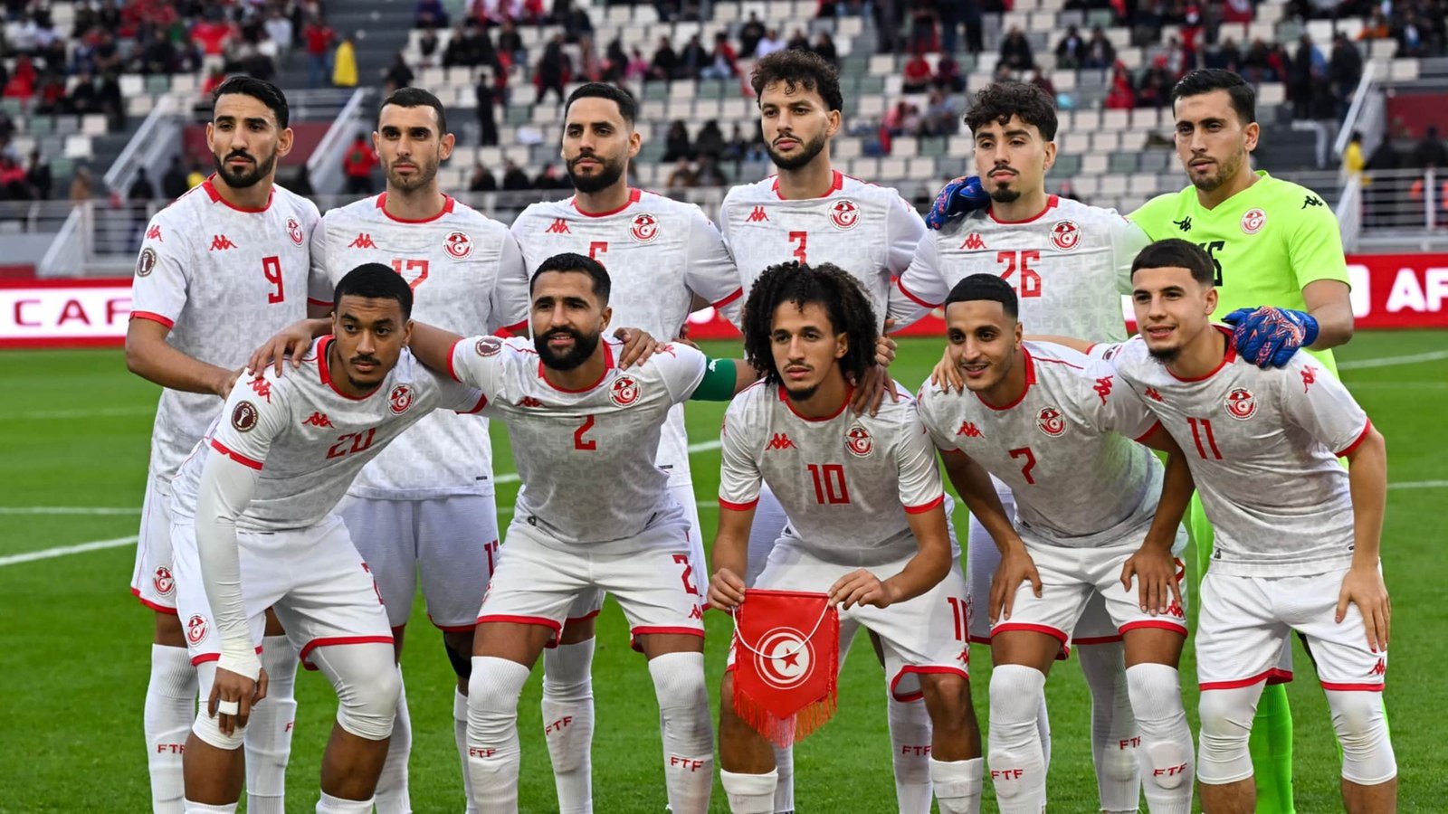 Tunisian national football team poses for a team photo, wearing white kits with red accents, displaying unity before a match.