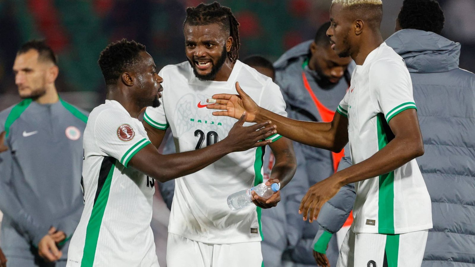 Players in green and white jerseys celebrate on the pitch, showcasing camaraderie after a match. The background features team members and a stadium atmosphere.