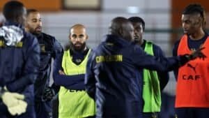 Footballeurs marocains en séance d'entraînement avec l'entraîneur, expressions concentrées, portant les tenues de l'équipe et des chasubles d'entraînement, prêts pour le prochain match.
