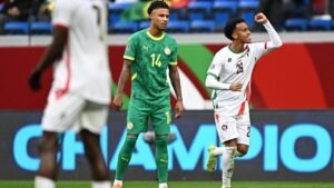 Moroccan player celebrating a goal with a clenched fist, while Senegalese player, in green kit, looks on in a tense moment of the match.