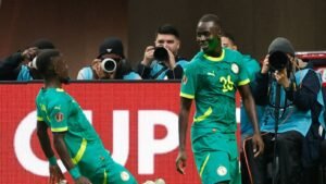 Senegalese spelers vieren een doelpunt, dragen groene tenues met gele accenten, terwijl fotografen het moment vastleggen op de achtergrond.