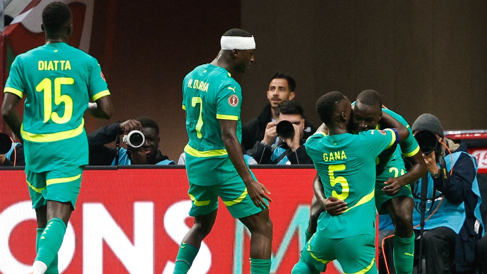 Les joueurs sénégalais célèbrent dans leurs kits verts vifs avec des accents jaunes, mettant en vedette Diatta, Gana et Oliviera, capturant un moment joyeux.