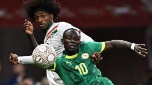 Sadio Mané, in green and yellow, battles for the ball against an opposing player in a tense match moment.