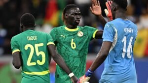 Senegal players Diouf (25) and Mendy (16) celebrate on the pitch, wearing vibrant green kits with yellow accents, conveying team spirit.