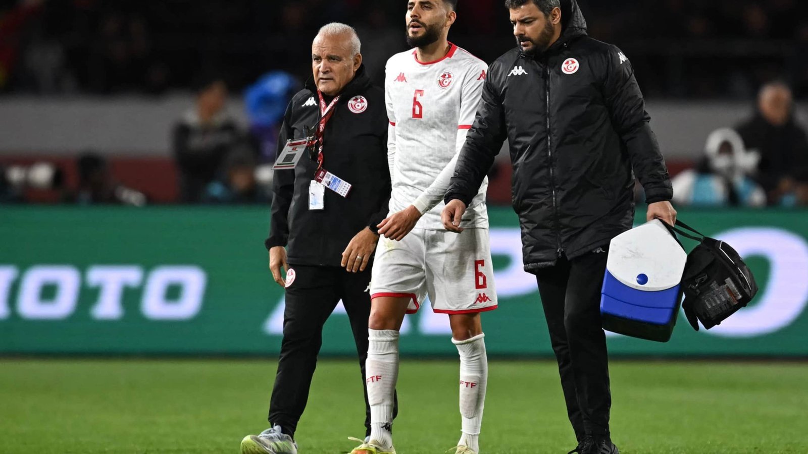 Tunisia's number 6 player is assisted off the pitch by coaching staff, showcasing concern and determination during a match.